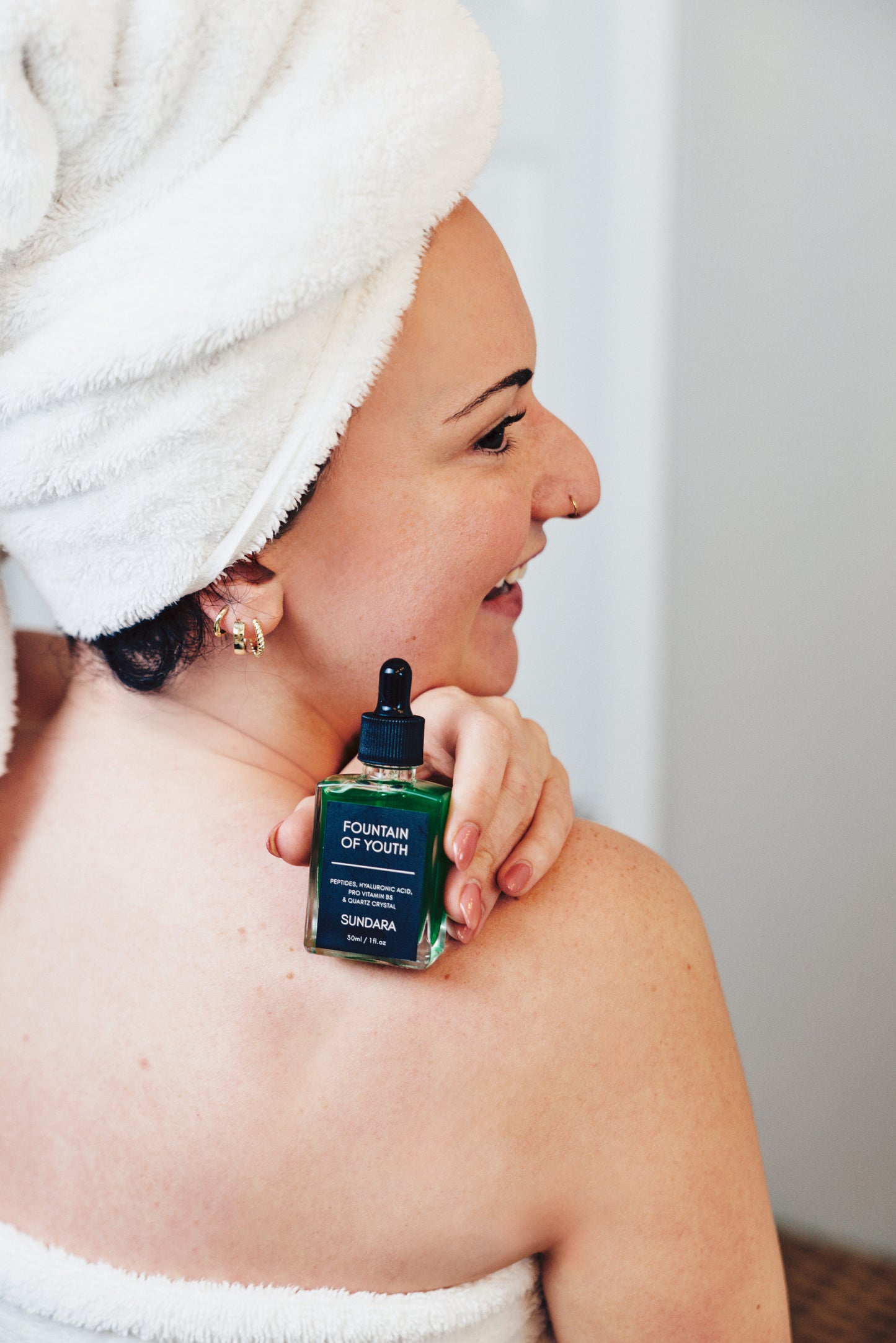 Woman with a towel wrapped around her head holding a bottle of soul of sundara