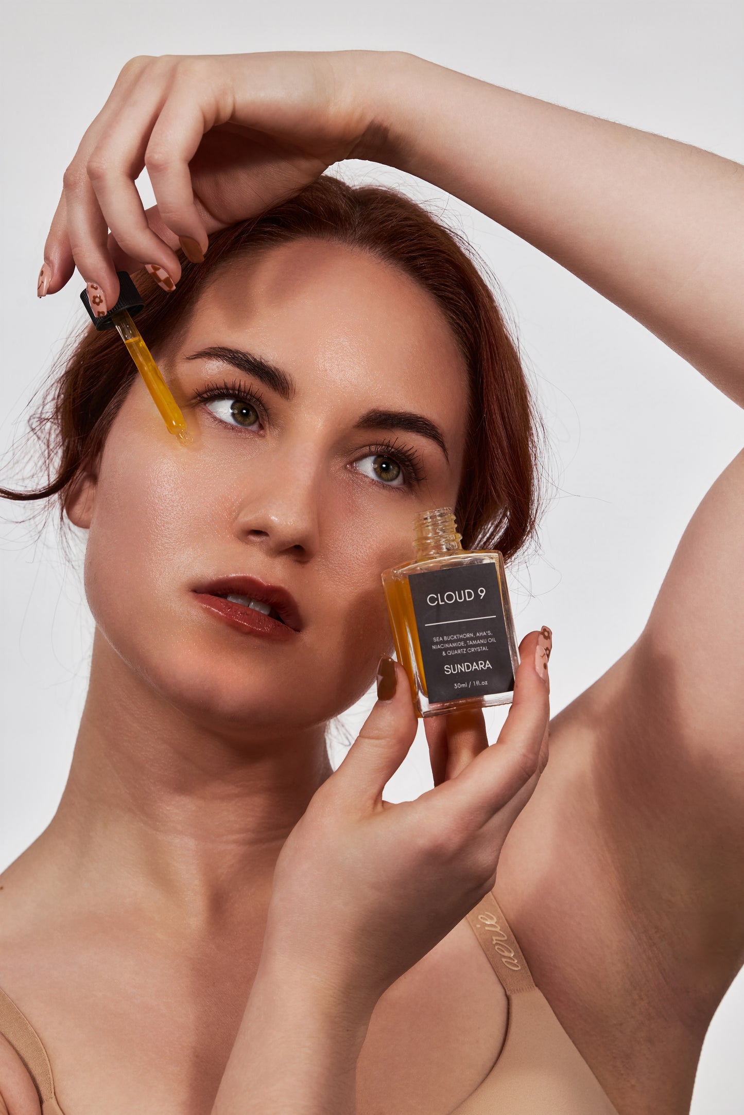 Woman applying a skincare product from a bottle labeled 'Cloud 9' on her face.