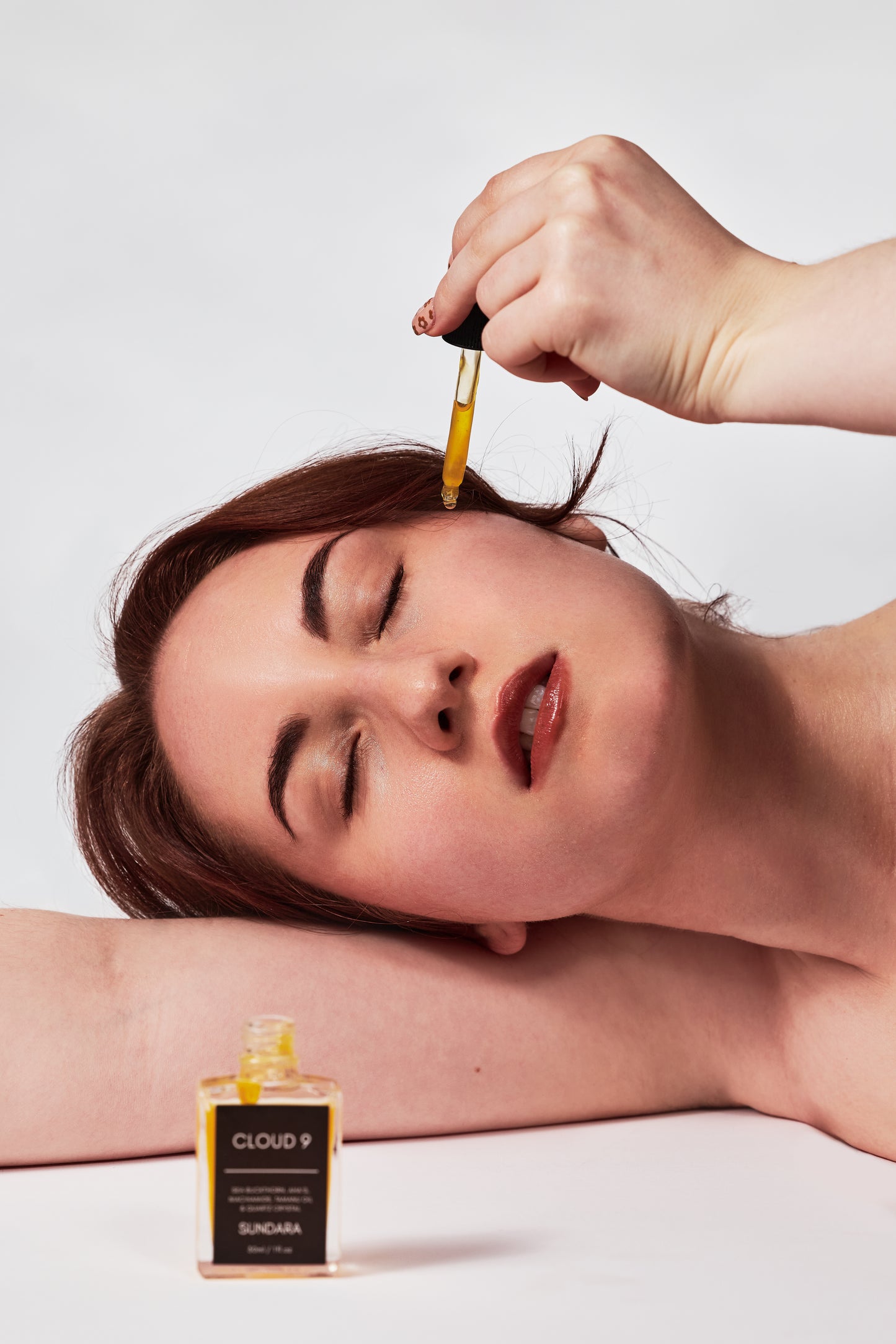 Person applying a dropper of liquid to their face with a bottle labeled 'Cloud 9' on a white background