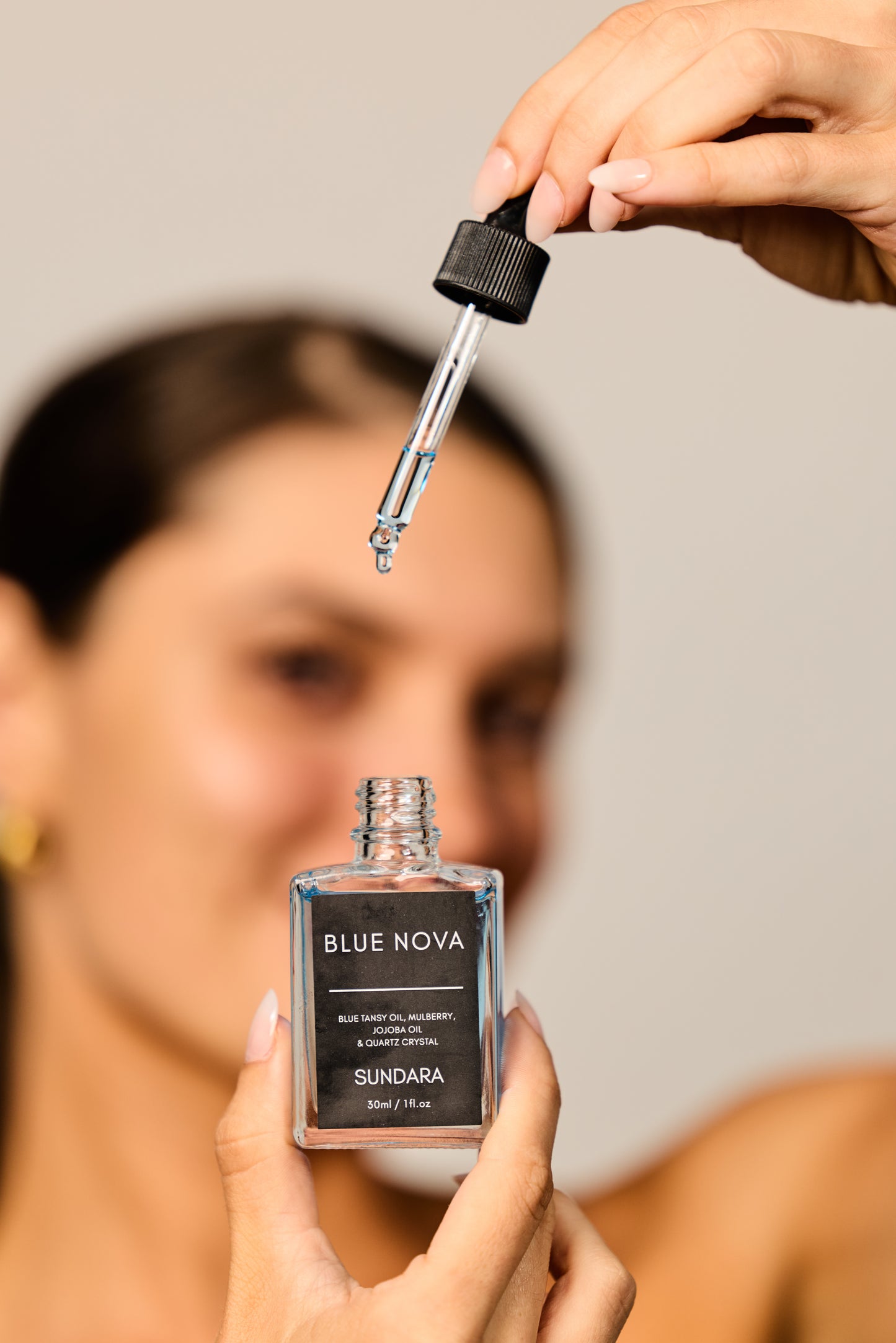 Person holding a Blue Nova Sundara skincare dropper bottle with a blurred background