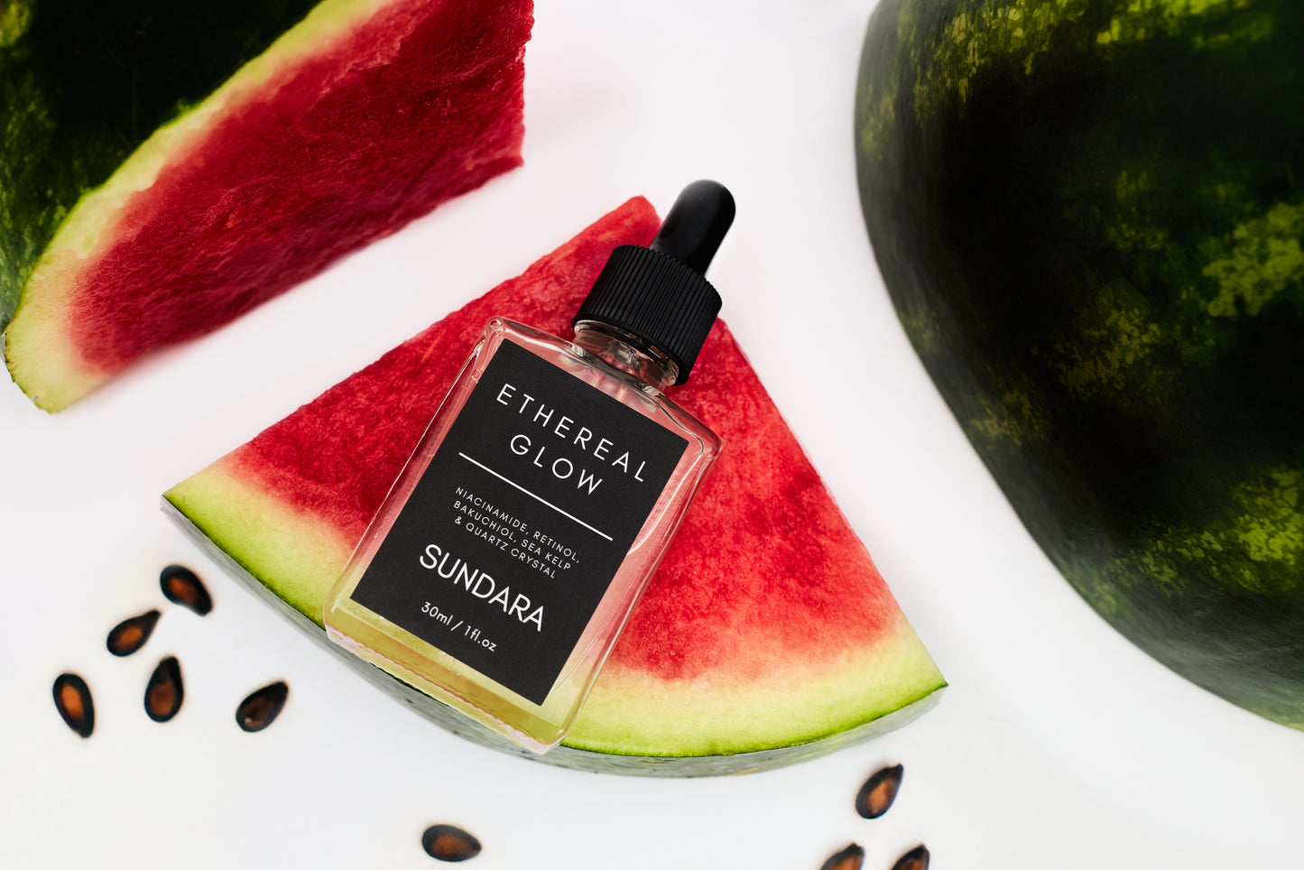 Bottle of 'Ethereal Glow Sundara' on a slice of watermelon with a whole watermelon in the background.