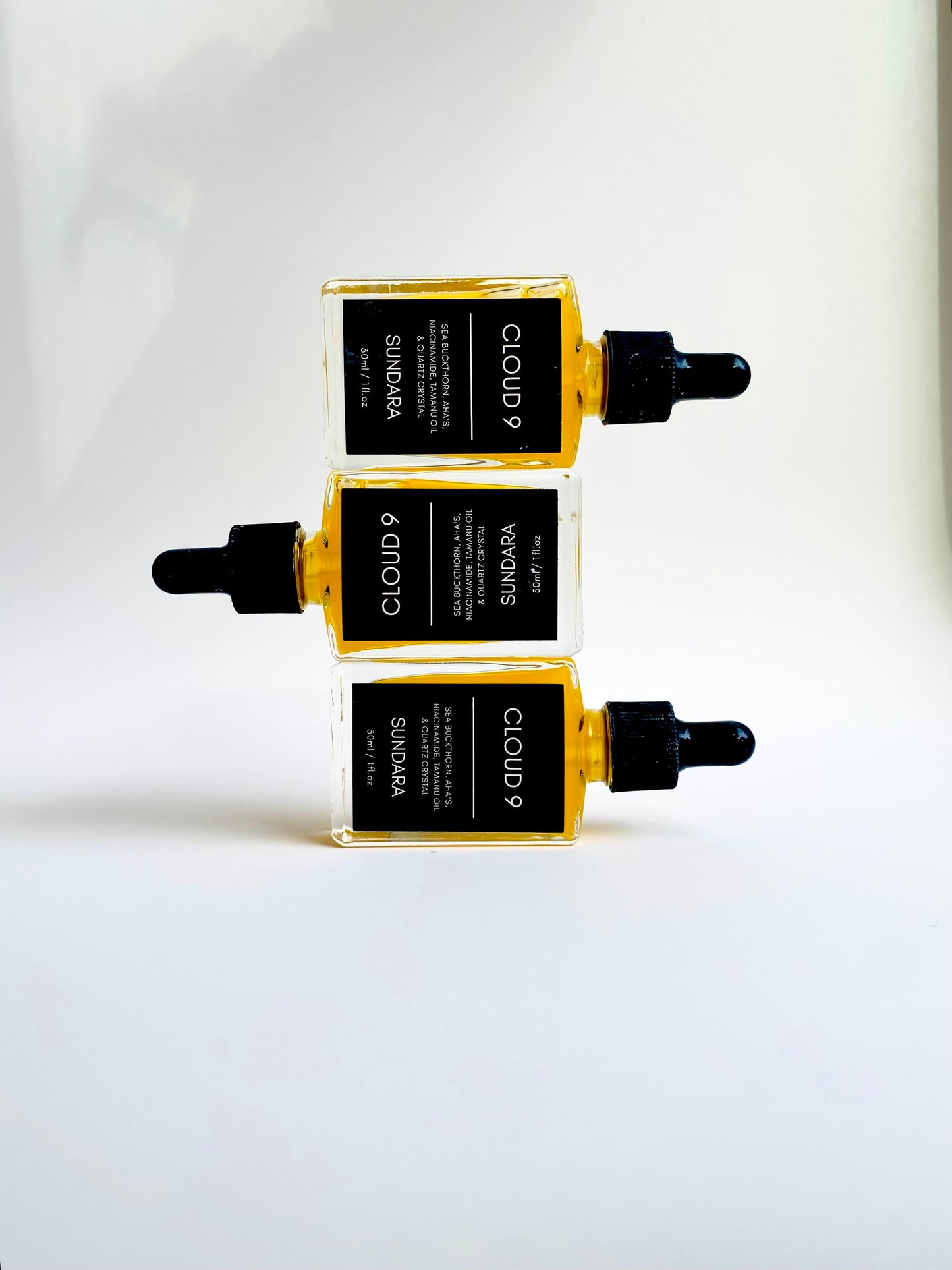 A bottle of 'Cloud 9' skin serum by Sundara, with a sea buckthorn oil dropper, placed on a surface with a crystal. Niacinimide, AHA's, Sea Buckthorn, Quartz Crystal for brightening, soothing, and repairing the skin barrier as an all natural, plant based, skincare serum.