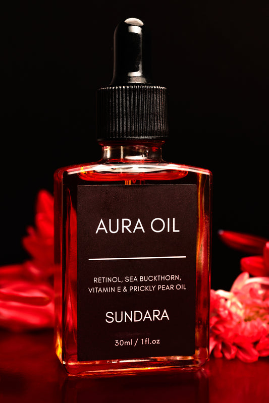 Bottle of Aura Oil with red flowers in the background