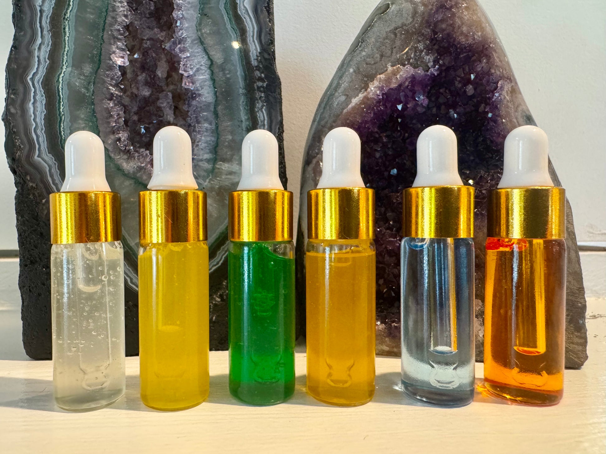 Set of six dropper bottles with gold caps in front of amethyst crystals. Sample organic all natural quartz crystal skincare