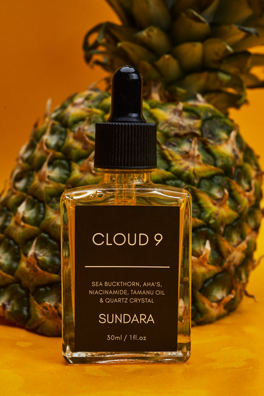 Bottle of Cloud 9 Sundara skincare product with a pineapple in the background